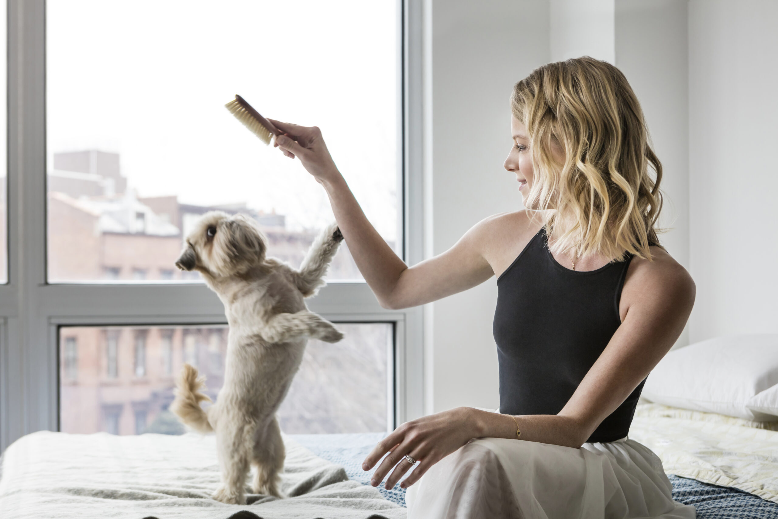 woman sitting on bed brushing her dog